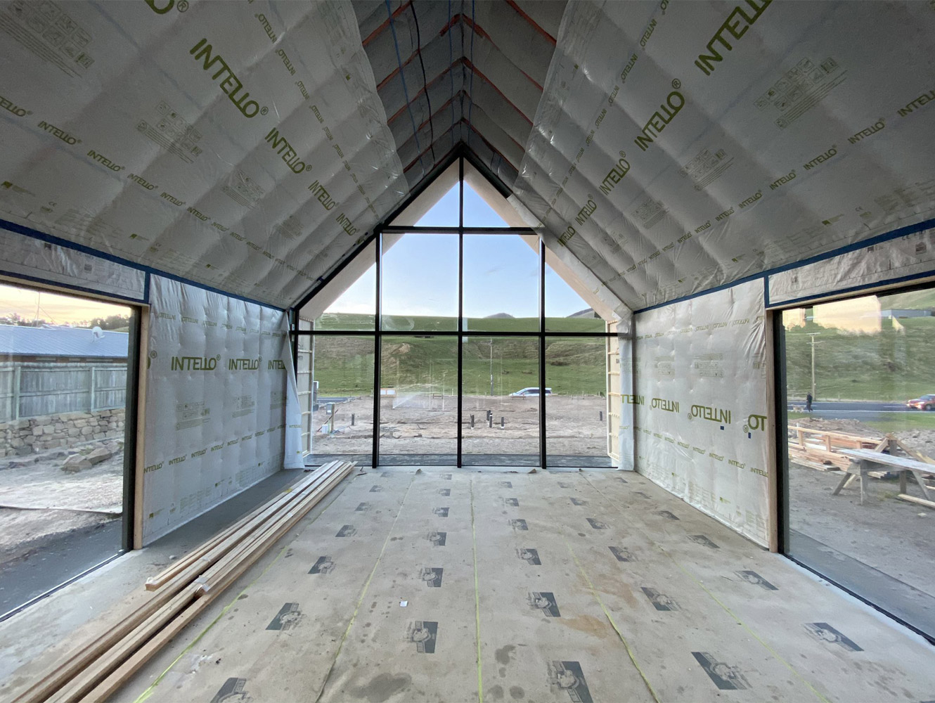 The inside of a new house being built with a big gabled floor to ceiling window at the end of the house