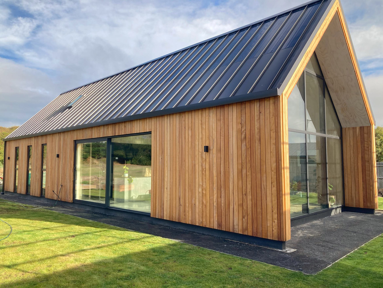 A photo of the exterior of a newly built house with wooden cladding and gabled black colour steel roof