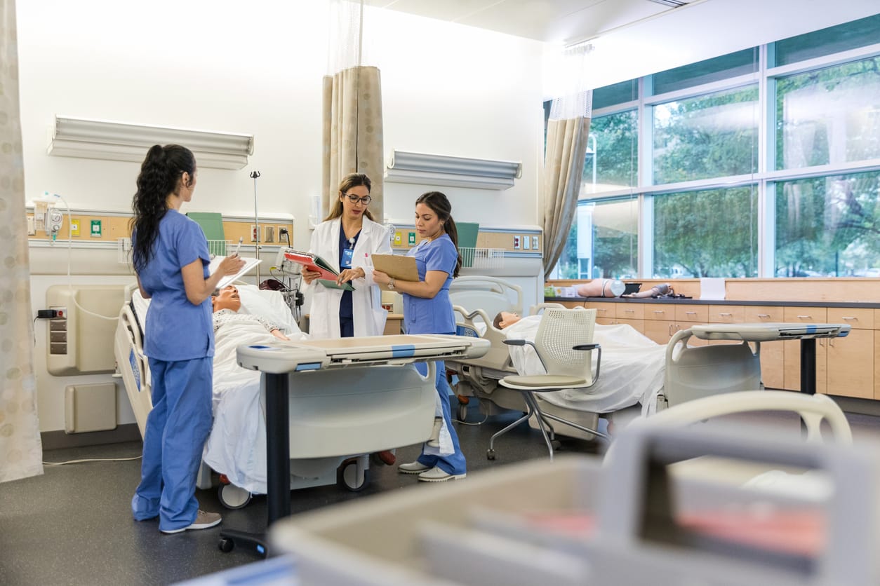 Two nursing students hold clipboards in a hospital room as they learn during their nursing school clinicals.