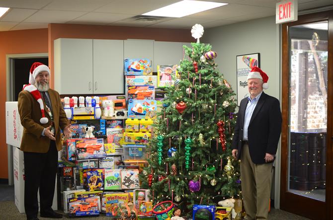 Shawn Slavin and Gary Crouch standing next to a large stack of toys and a christmas tree