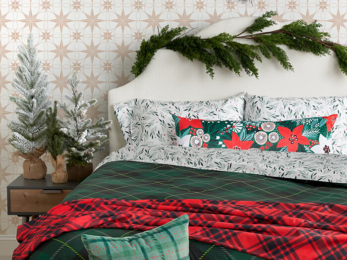 Festive bedding in red and green against a tan, starburst wallpaper. Greenery decorates the headboard and side table.