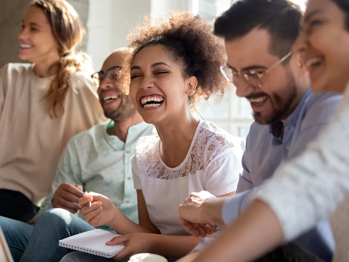 Happy group of diverse young people sitting in a row having fun, laughing, and taking notes.