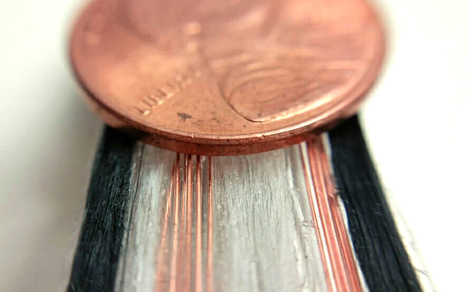 Extreme closeup of multi-channel multi-material ribbon of continuous fiber. A penny laid on top to show scale.