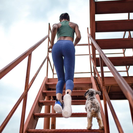 woman in athletic outdoor voices apparel running up metal staircase next to small dog