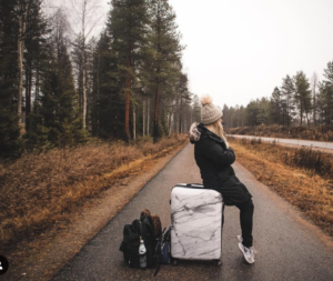 woman sitting on suitcase in road Kylee Nelson passportsandpreemies