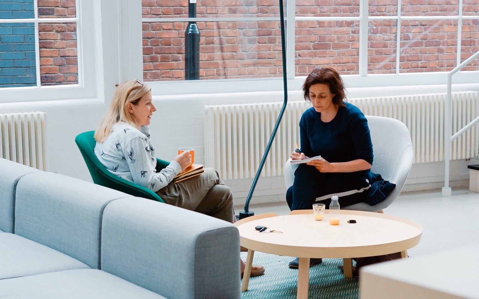 two woman sit on sofa chairs inside home studying