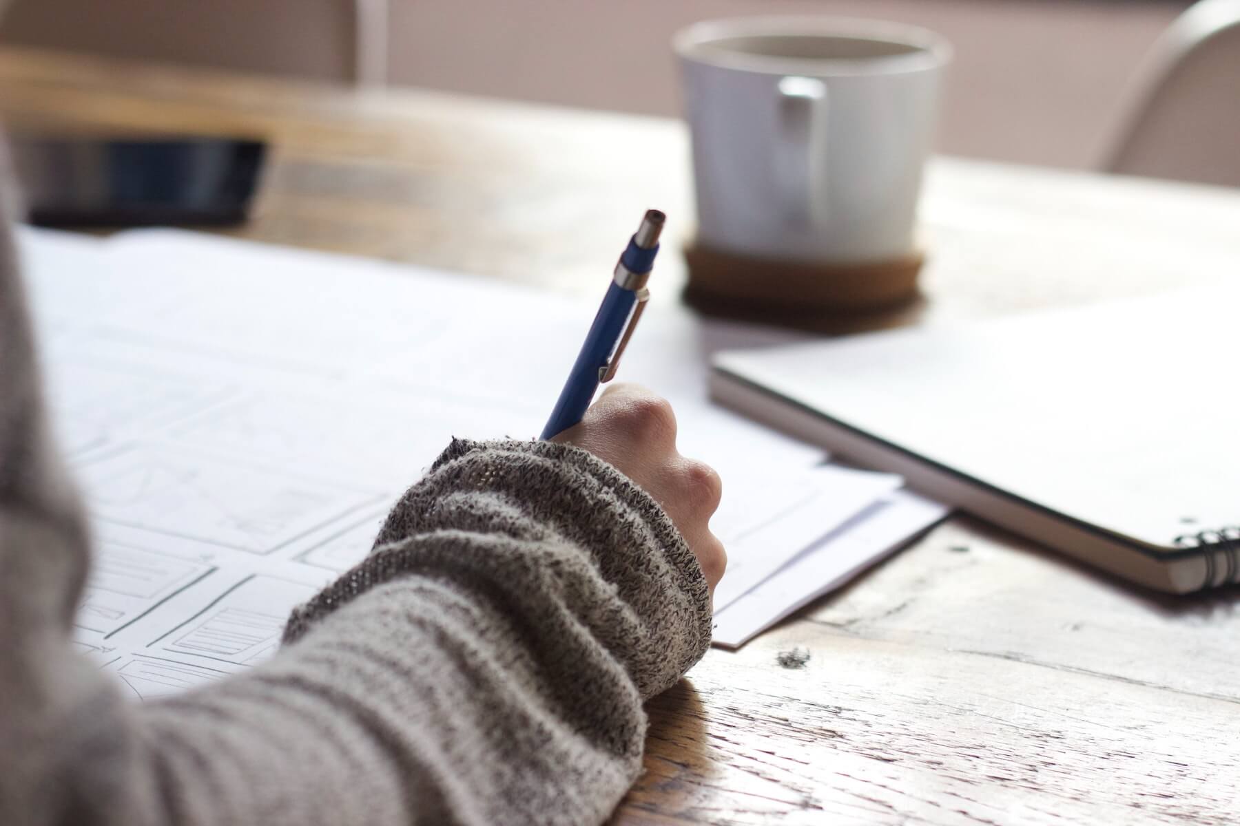 woman holding pencil sitting at cafe table with coffee and writing notes studying new grad nurse nursing