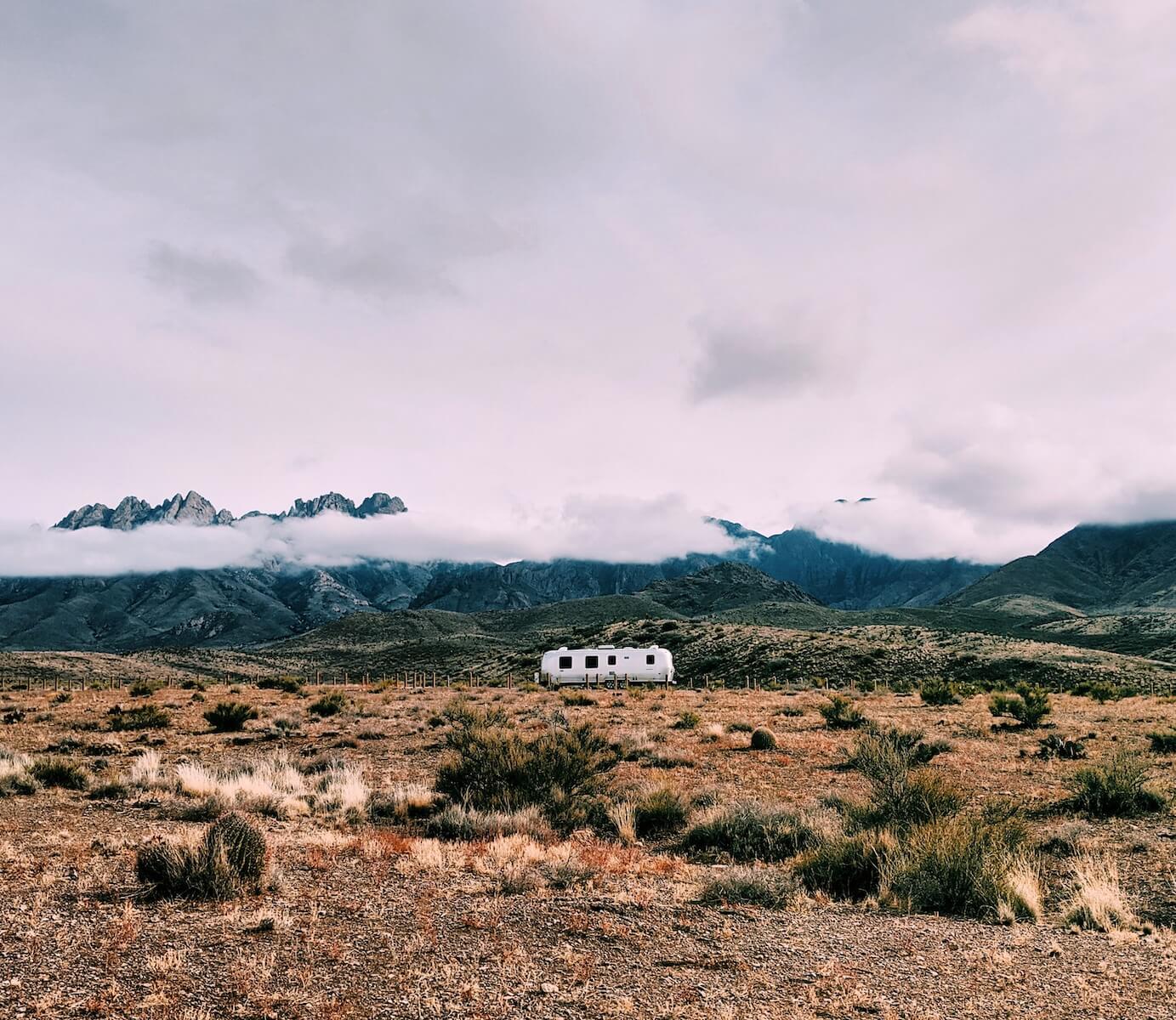 airstream RV on desertscape with mountains shrouded in clouds in the background travel nursing in an RV