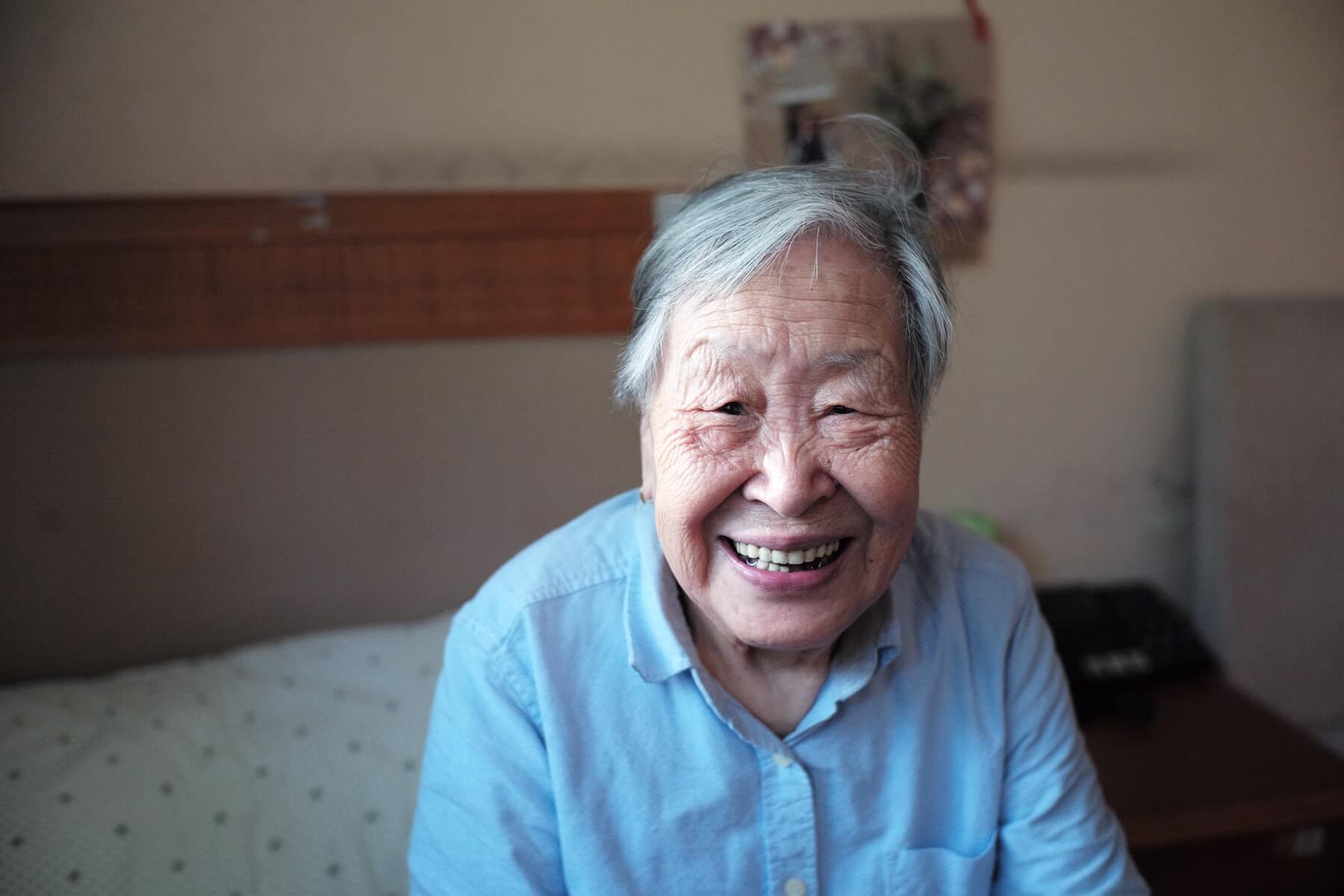 elderly woman sitting on bed and smiling into camera