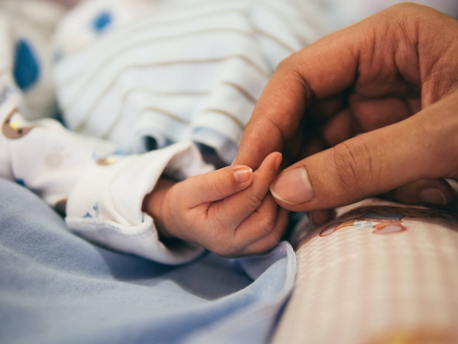 baby in NICU holding adult hand critical care nurse