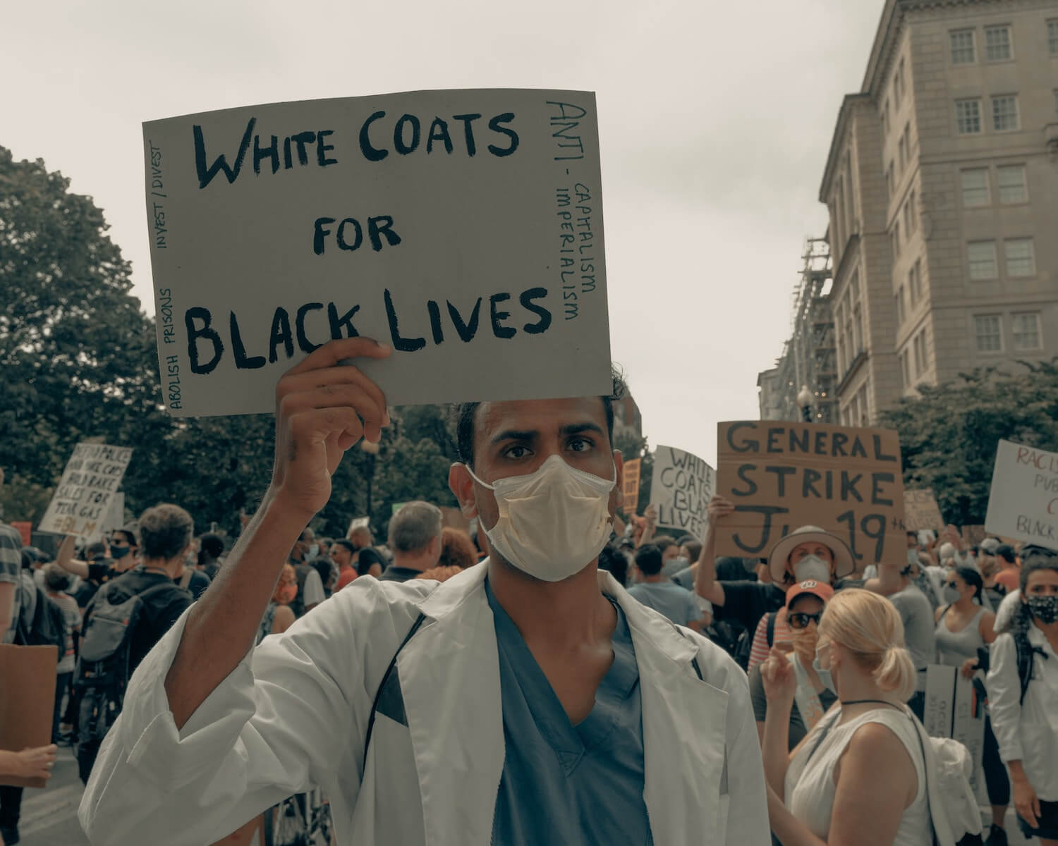 man at BLM protest holding white coats for black lives sign racial bias in healthcare healthcare disparity