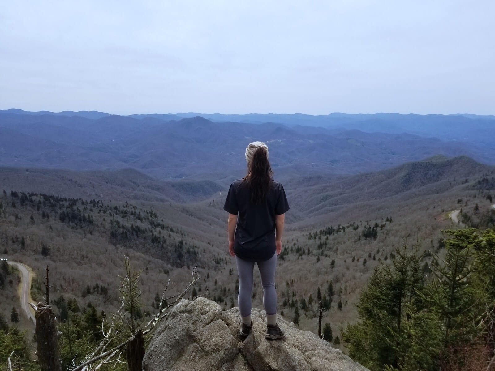 woman standing on cliff overlooking mountainous valley wilderness nursing
