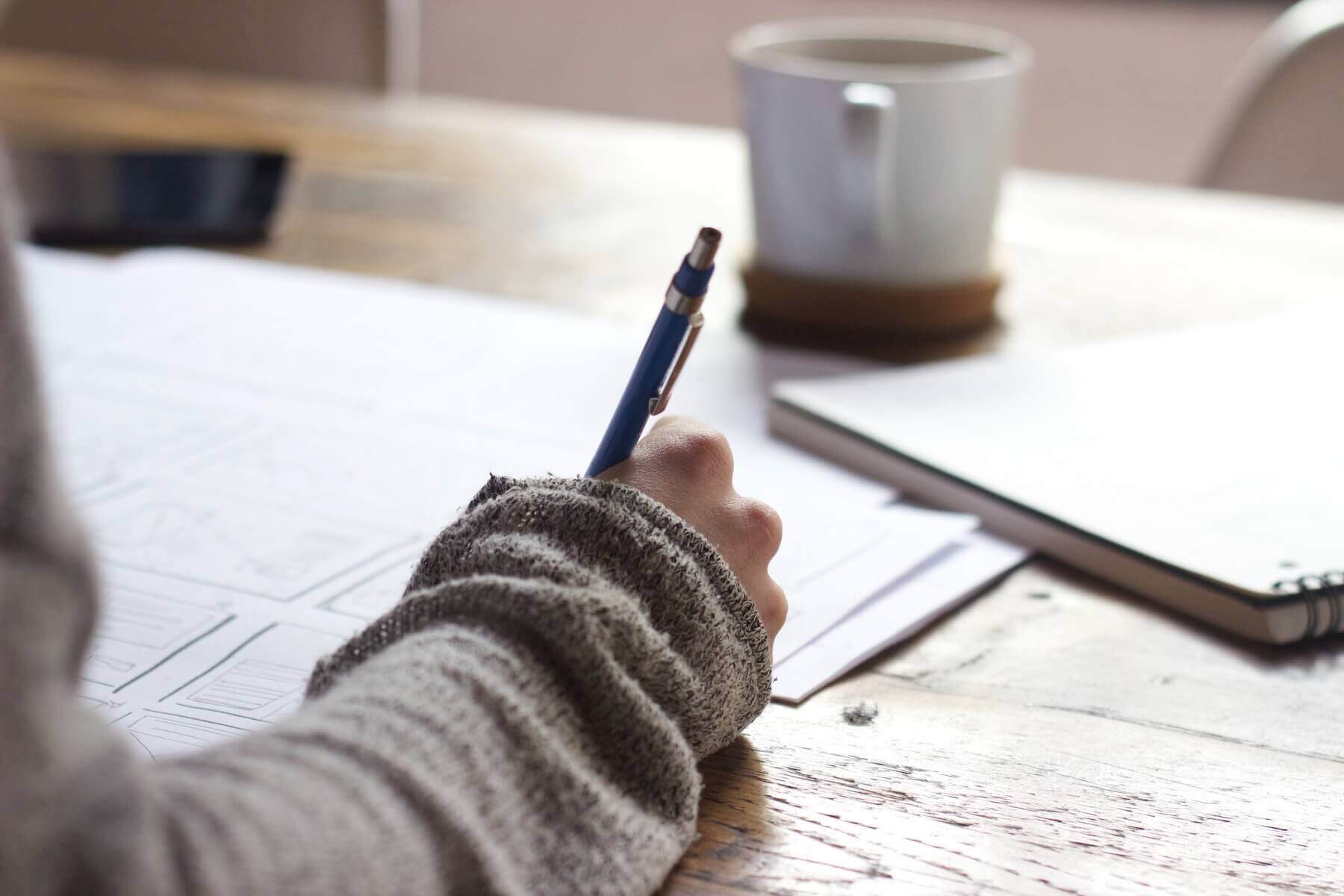 woman holding pencil sitting at cafe table with coffee and writing notes studying new grad nurse nursing