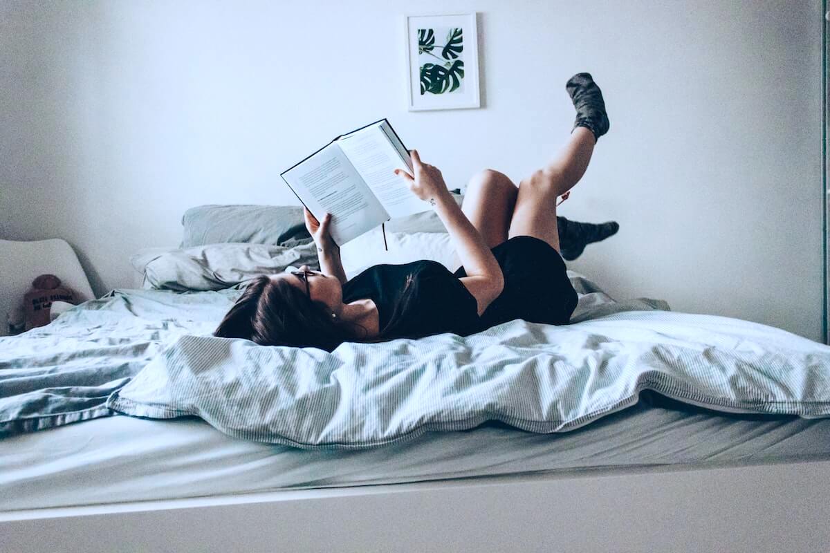 woman lying in bed with nursing textbook studying at home