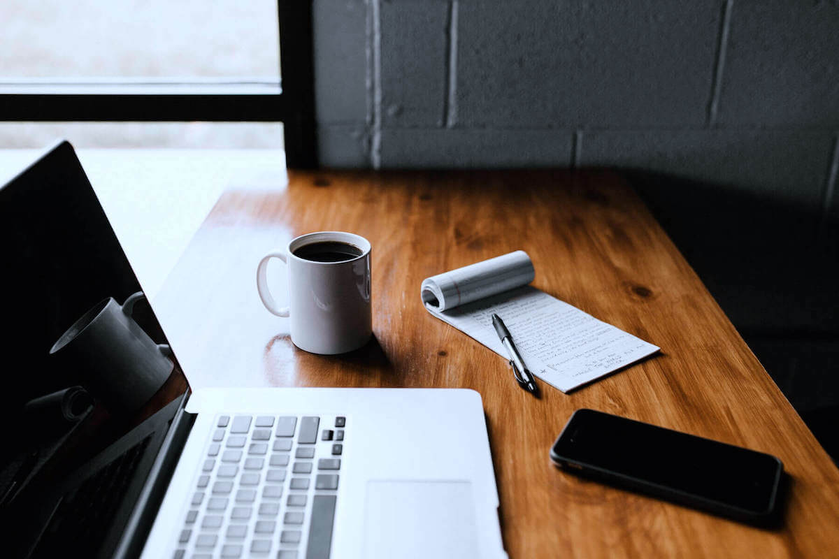 laptop on table next to coffee cup notepad and iphone work from home setup remote nursing jobs from home