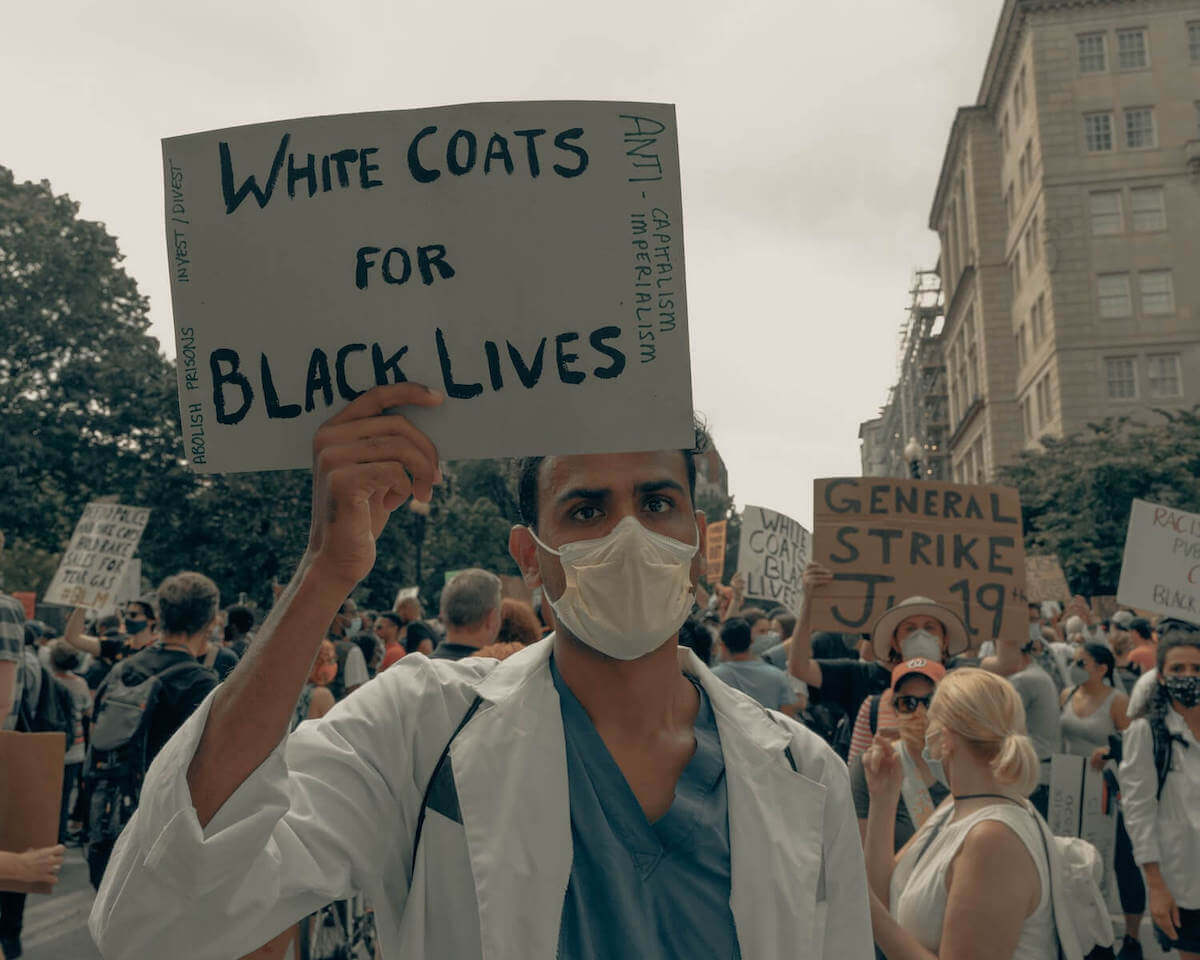 man at BLM protest holding white coats for black lives sign racial bias in healthcare healthcare disparity