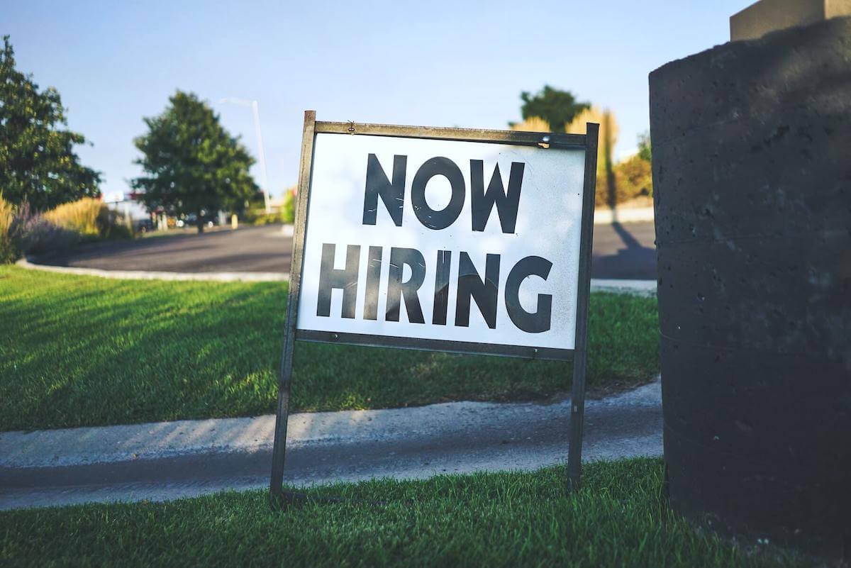 now hiring sign on grass field near street hiring for nursing jobs