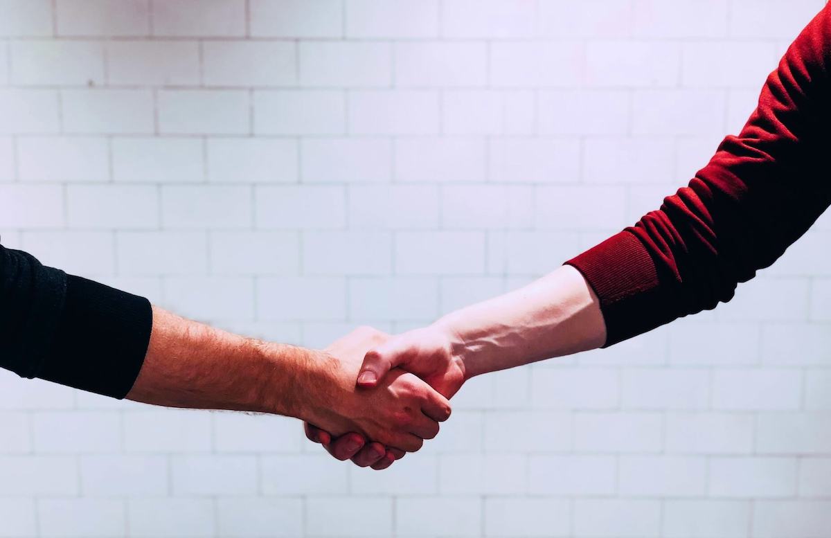 two men shaking hands in front of white wall travel nurse contract