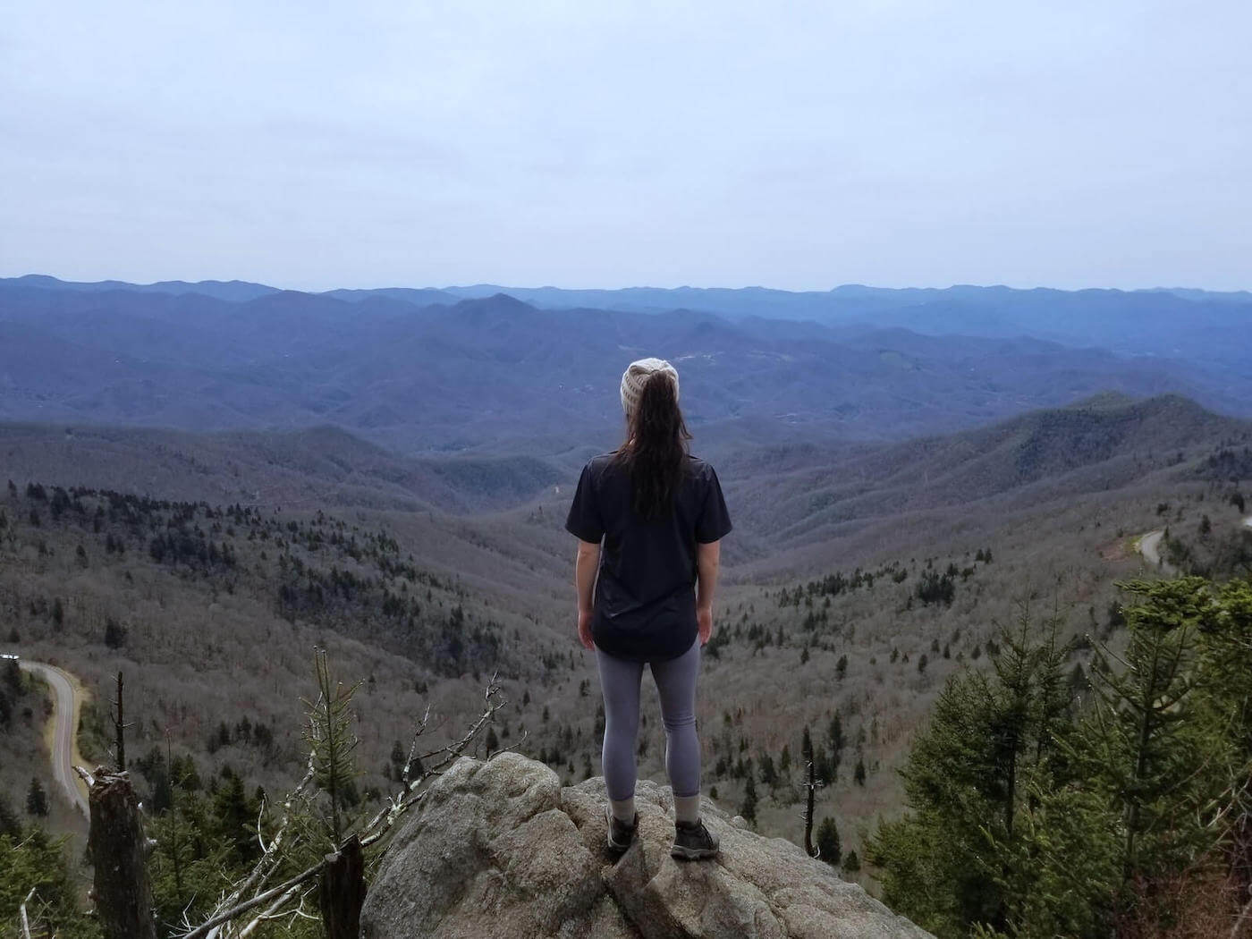 woman standing on cliff overlooking mountainous valley wilderness nursing