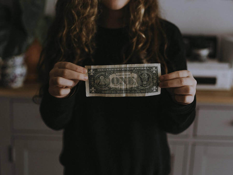 woman in black sweater holding dollar bill in front of her budgeting for nurses