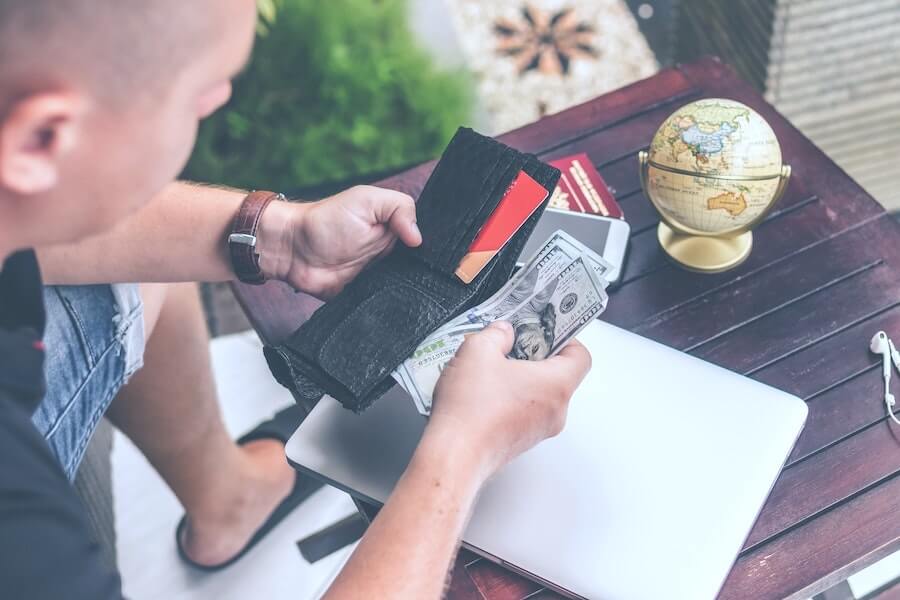 man looking at wallet and money sitting over desk with computer passport and globe staff nurse to travel nurse