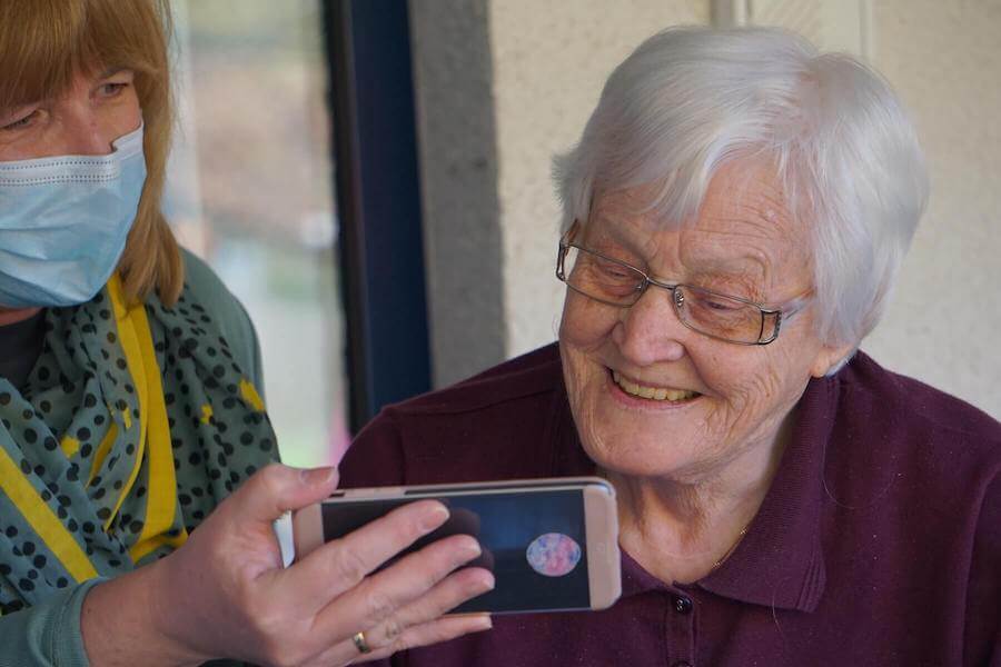 home health nurse with mask on shows elderly woman something on her phone home health nursing