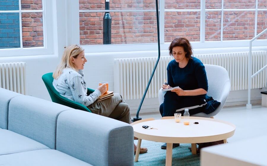 two woman sit on sofa chairs inside home studying nursing interview