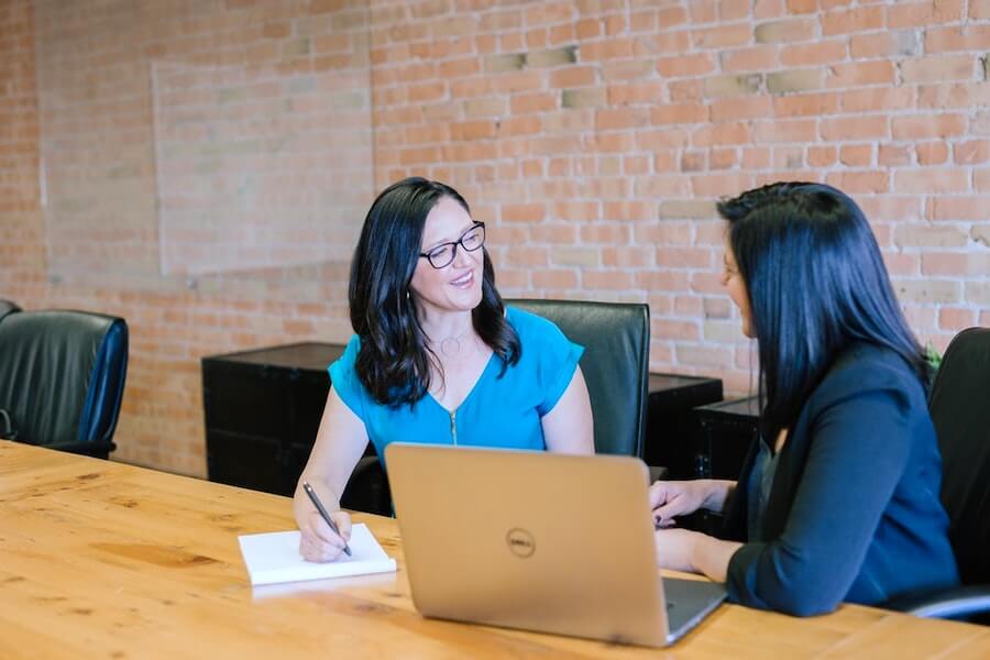 woman in teal t-shirt sitting beside woman in suit jacket nursing interview