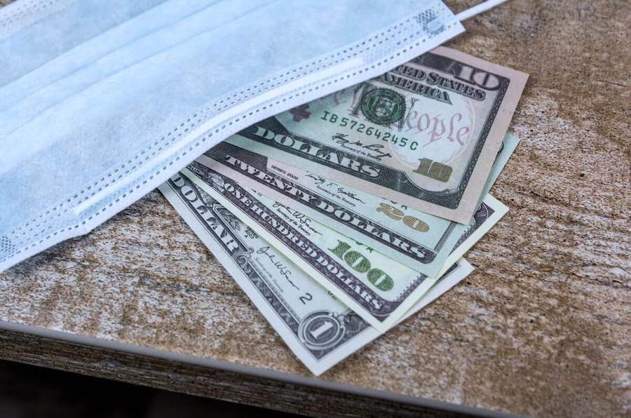 surgical mask laying on top of US money on a table how much do nurses make