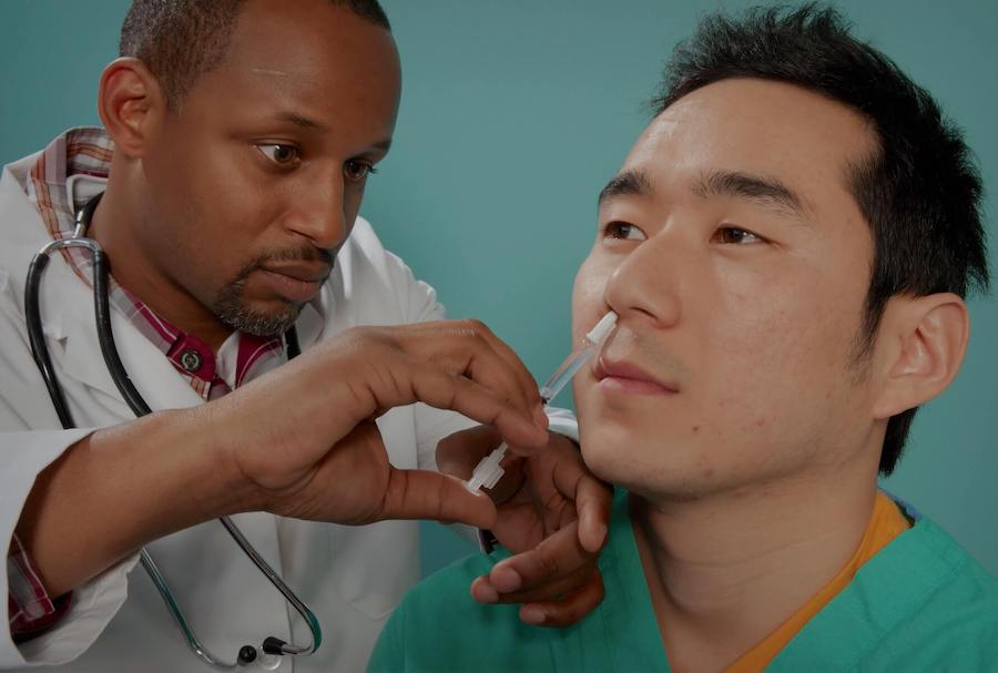 nurse practitioner gives vaccine to man on the right through is nasal cavity FNP