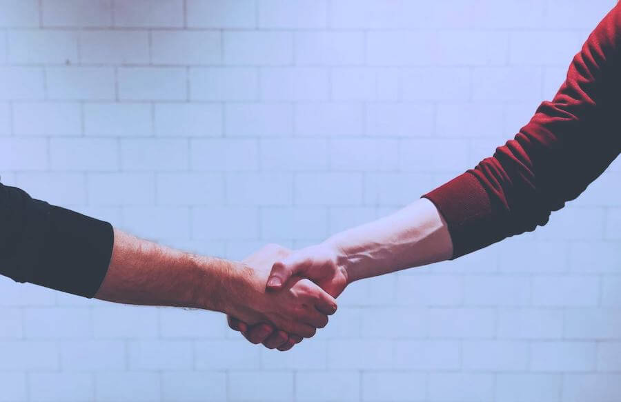 two men shaking hands in front of white wall travel nurse contract