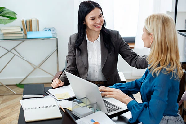 Smiling female employees using laptop working together