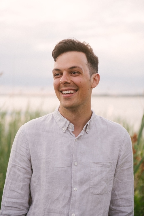 a picture of man in a collared shirt with grasses and a setting sun  in the background