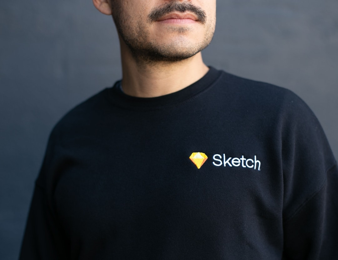 man with moustach wearing black sweater with sketch embroidery 