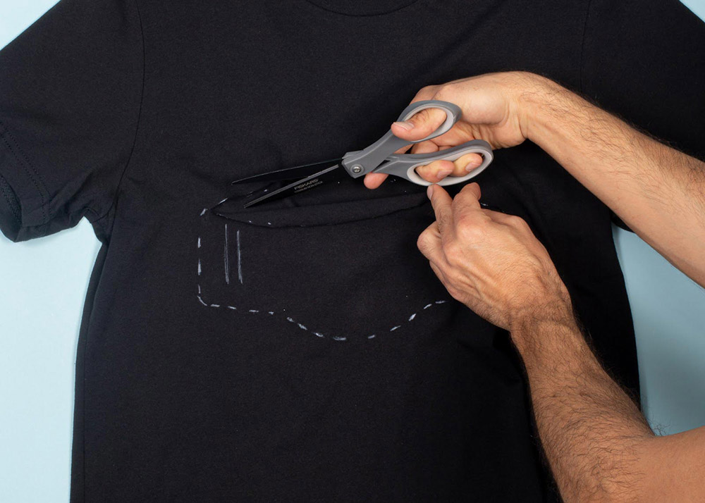 man cutting outline of face mask out of a shirt