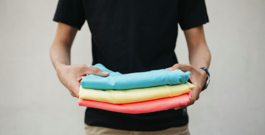 Dru holding stack of colored shirts