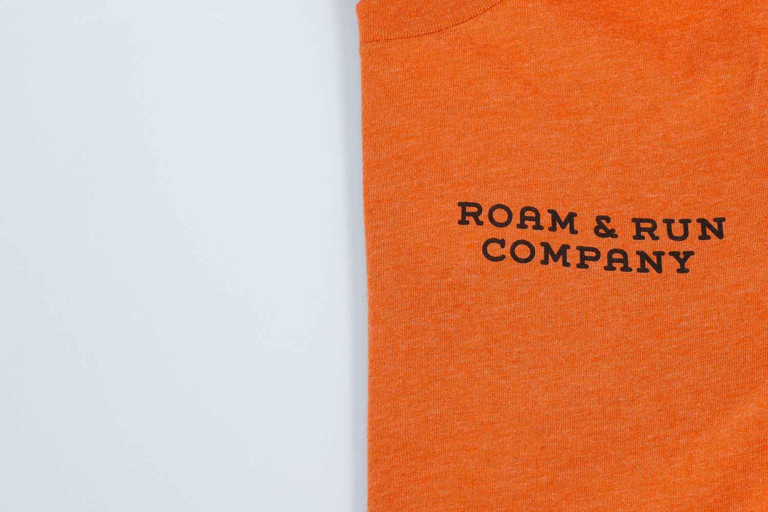 Orange shirt folded in half with "roam & run company" in black text on it