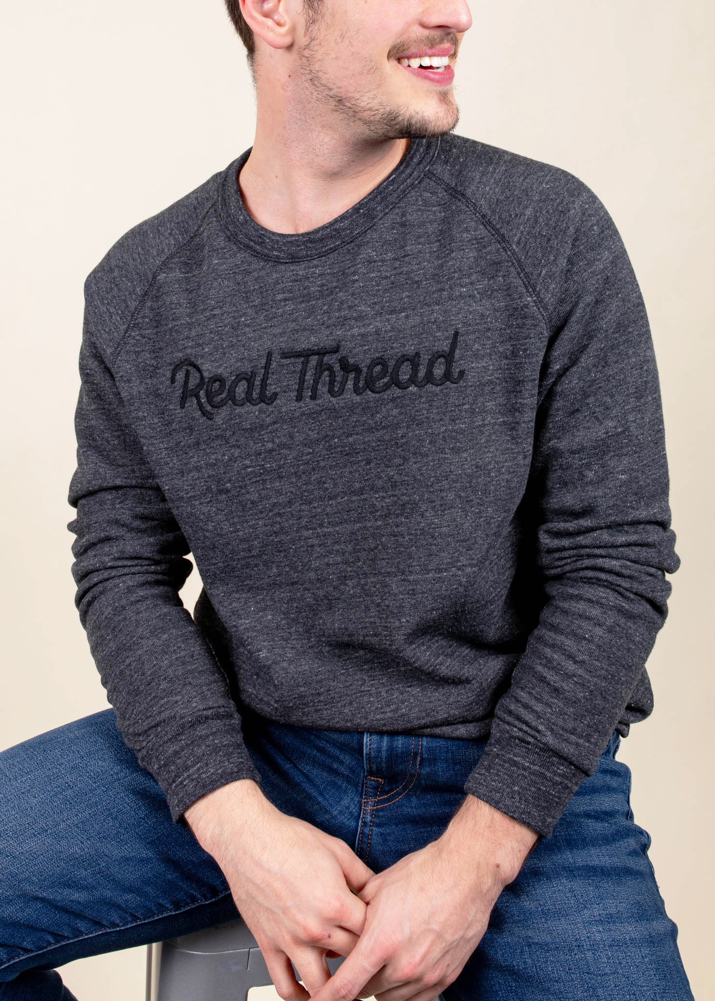 Smiling man wearing a grey sweatshirt with "Real Thread" embroidered in black on the chest