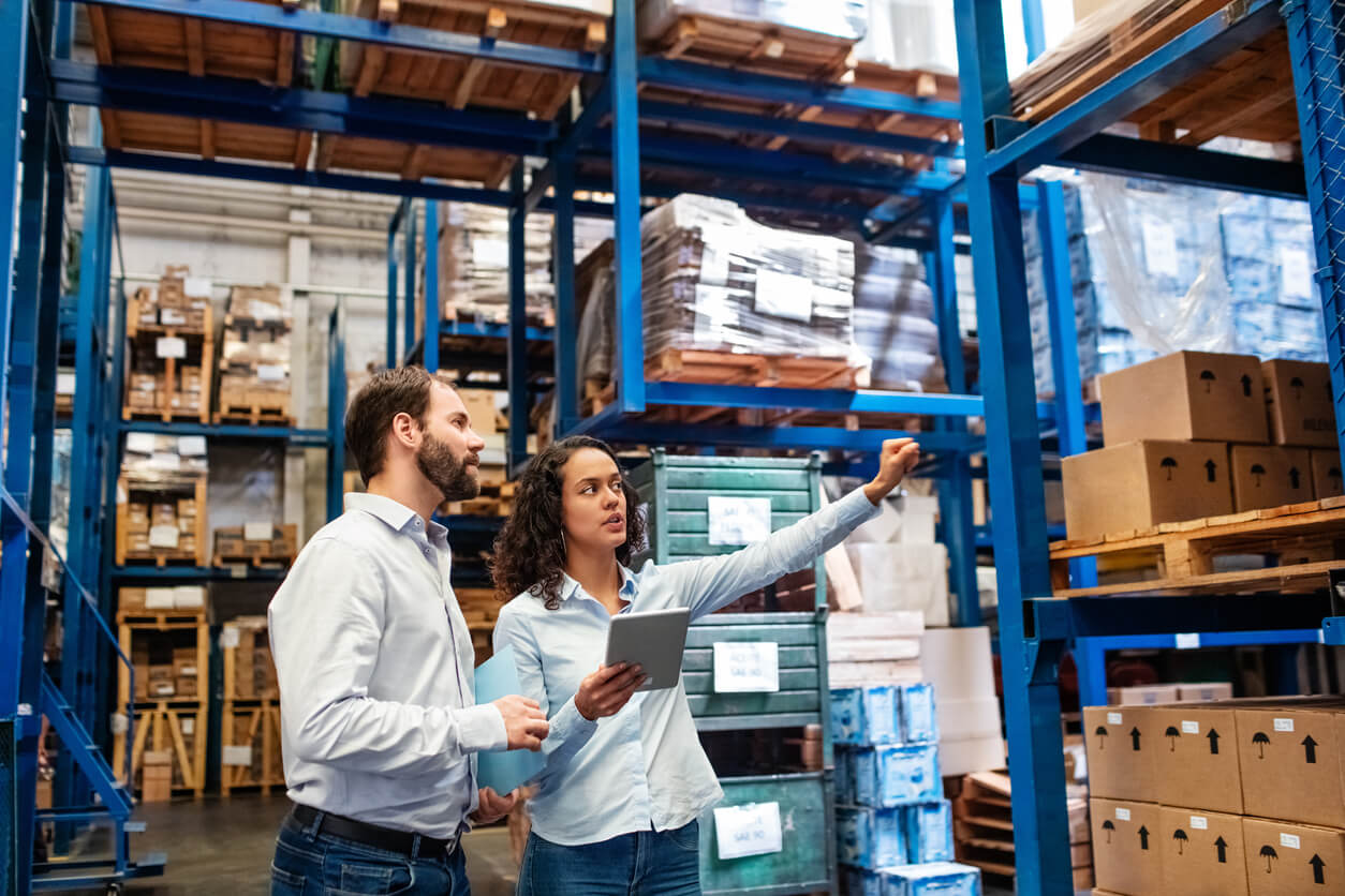 A woman with a smart tablet shows a man around an inventory warehouse/