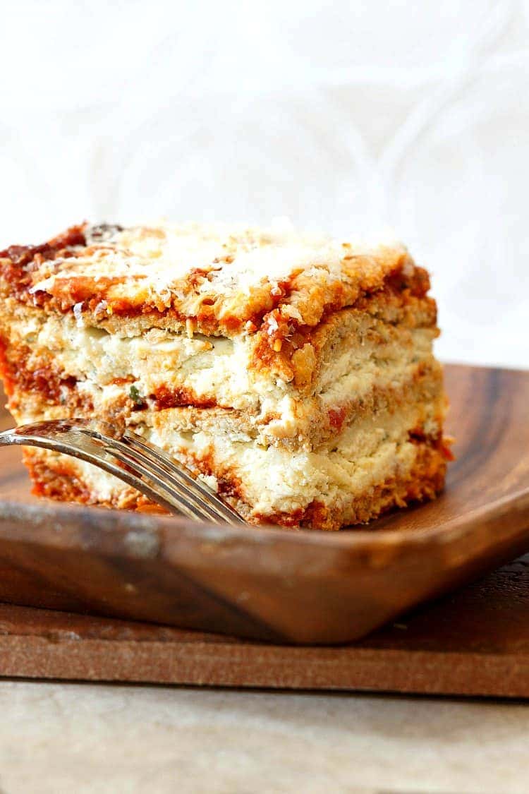 Une grosse part de lasagnes de chou-fleur est posée sur une assiette en bois. Une fourchette se trouve à côté en attente de dégustation.