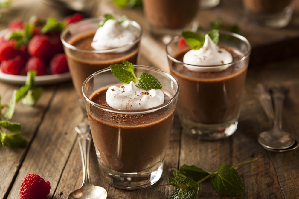 Sur une table en bois, sont disposés trois verrines contenant la mousse au chocolat. Le topping est composé de crème fraîche et feuilles de menthe.