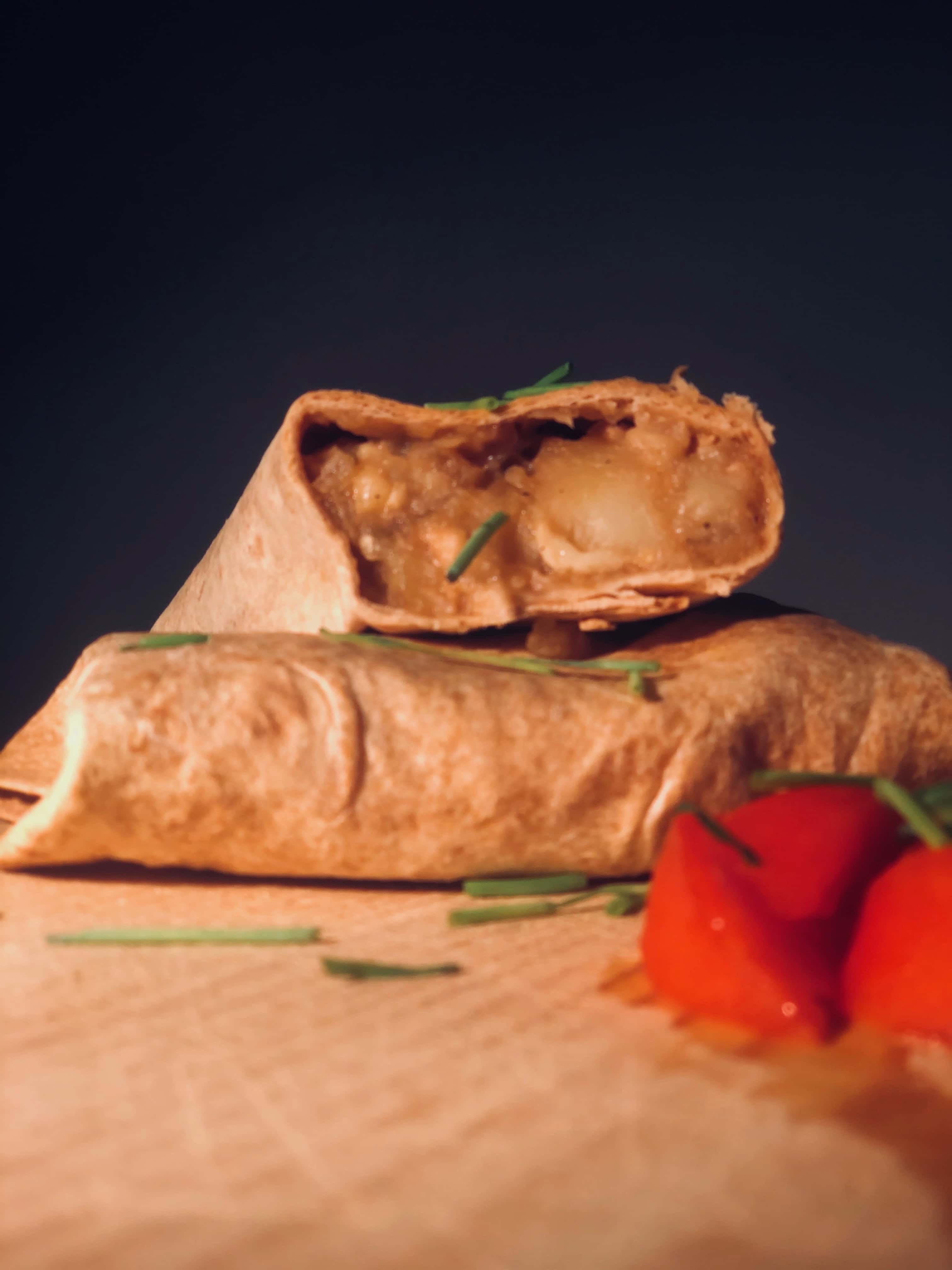 Deux gros french tacos montagnards sont posés sur une planche à découper en bois. L'un des deux montre la généreuse garniture à base de viande.