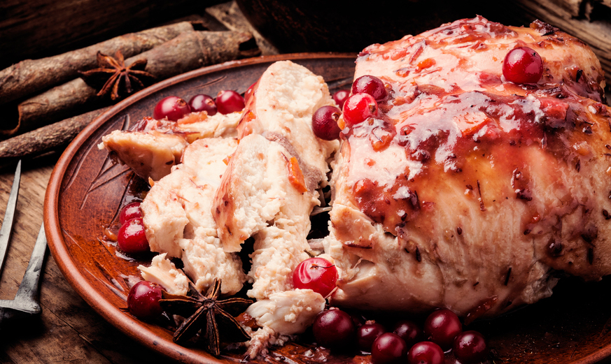 Dans un plat en terre cuite ovale, se trouve les escalopes de poulet qui sont accompagnées par un grand nombres de cranberry.