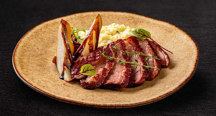 Sur une assiette de couleur beige, les filets de canard sont arrangés de manière à simuler un petit lapin. A côté se trouve les poires.