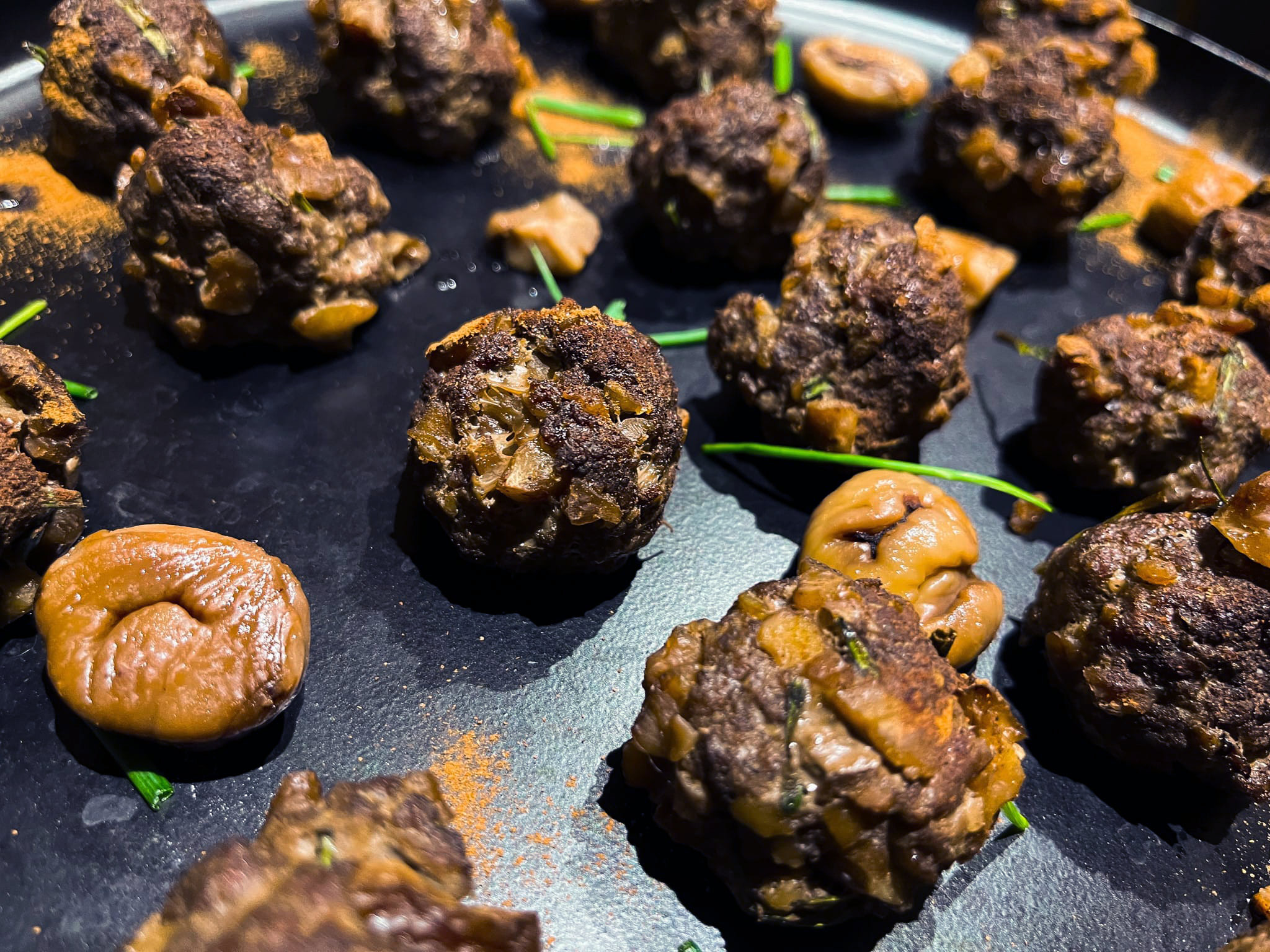 Sur une plaque de cuisson se trouve les boulettes de boeuf bien grillées ainsi que des marrons.