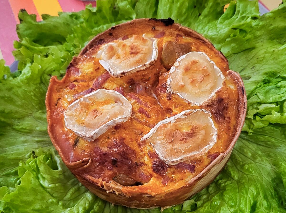 Sur une salade verte, un grand wrap accueille quatre petites quiches avec de la ratatouille, du bacon et du fromage de chèvre.