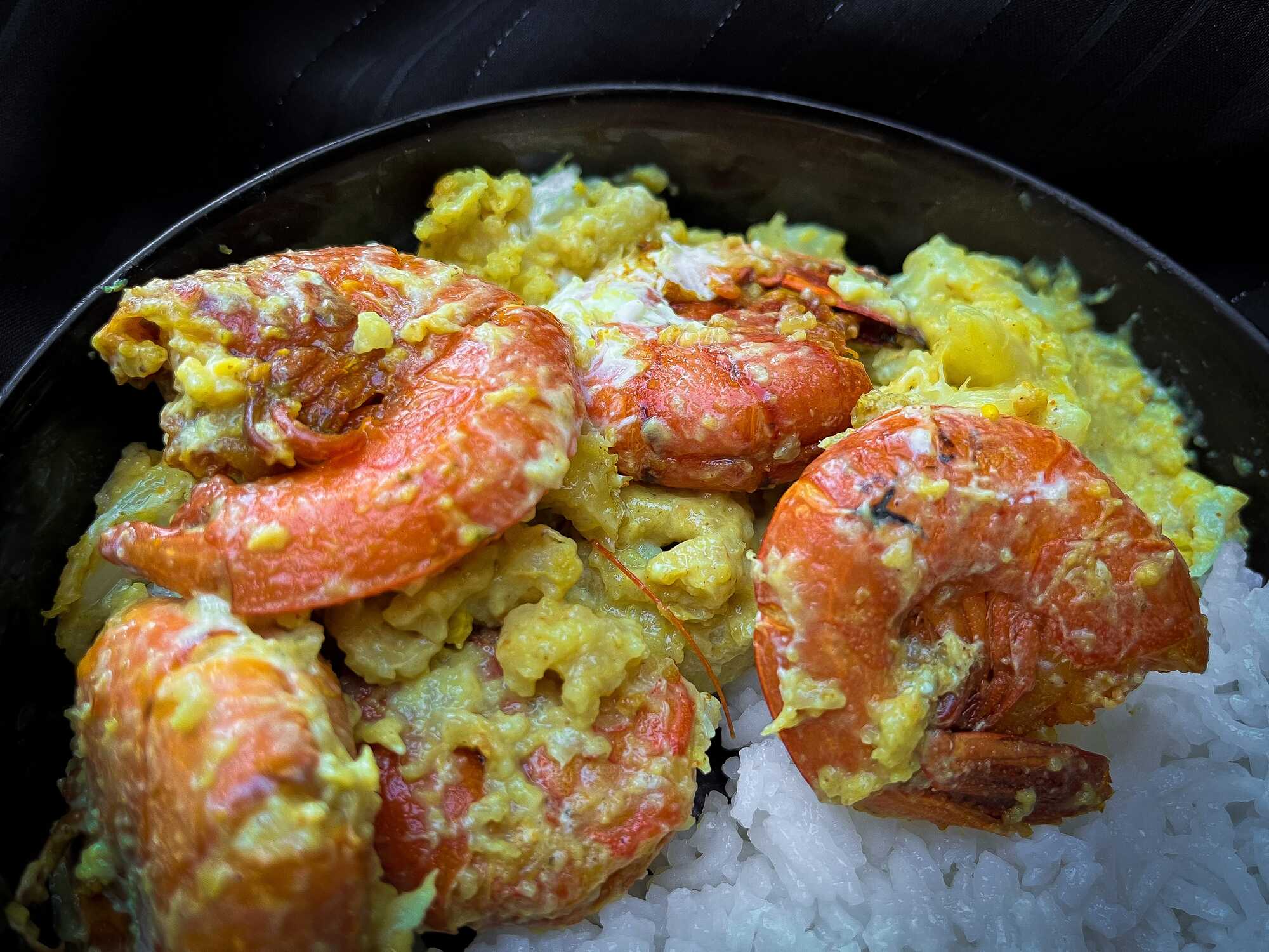 Dans un saladier se trouve cinq grosses crevettes mélangées avec du curry et du miel, accompagné de chou-fleur.