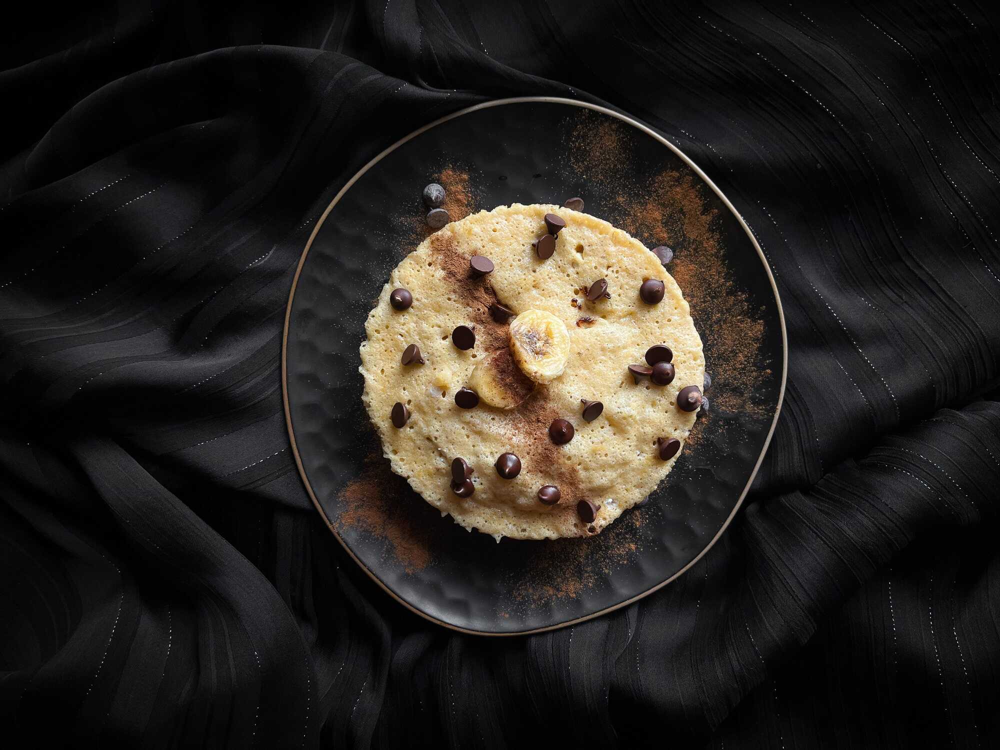 Le banana bread protéiné est présenté dans un petit bol . Le topping est assuré avec deux petites tranches de banane et des pépites de chocolat.