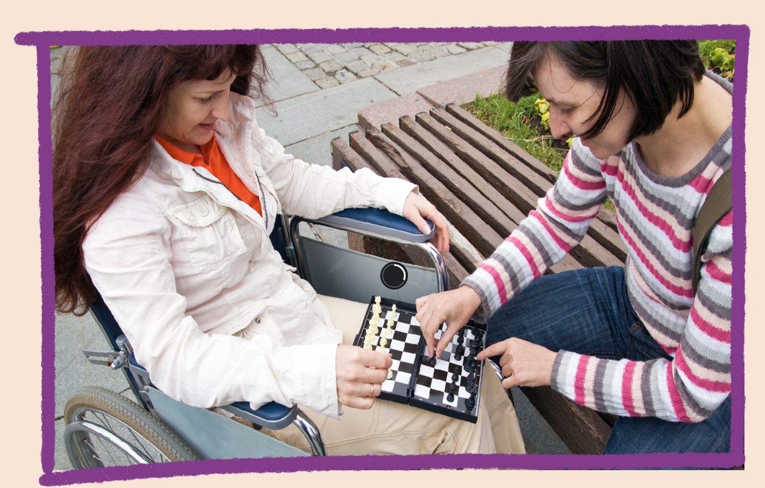 Photo of two women playing chess in a park. One is in a wheelchair and the other is sitting on a park bench.