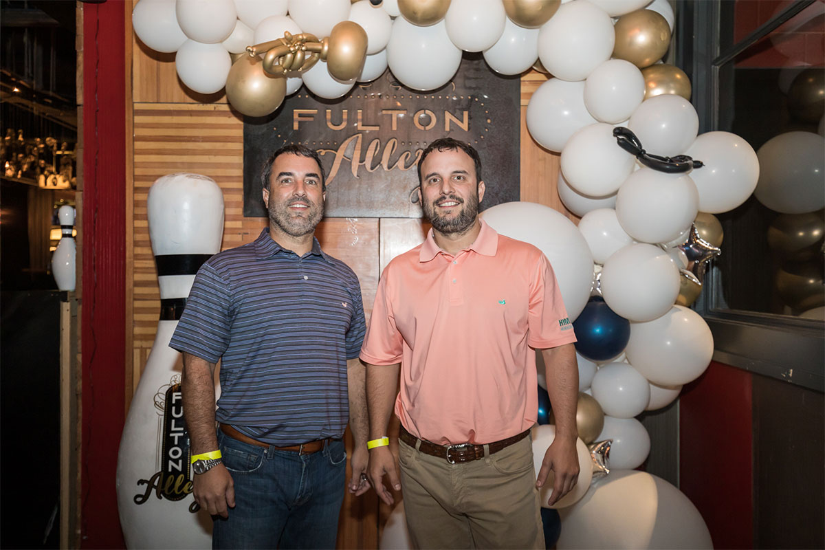 Jay and Chad Himmel in front of a Fulton Alley bowling sign with balloons around them